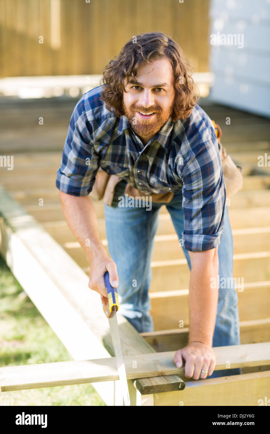 Confident Worker Cutting Wood With Saw At Construction Site Stock Photo