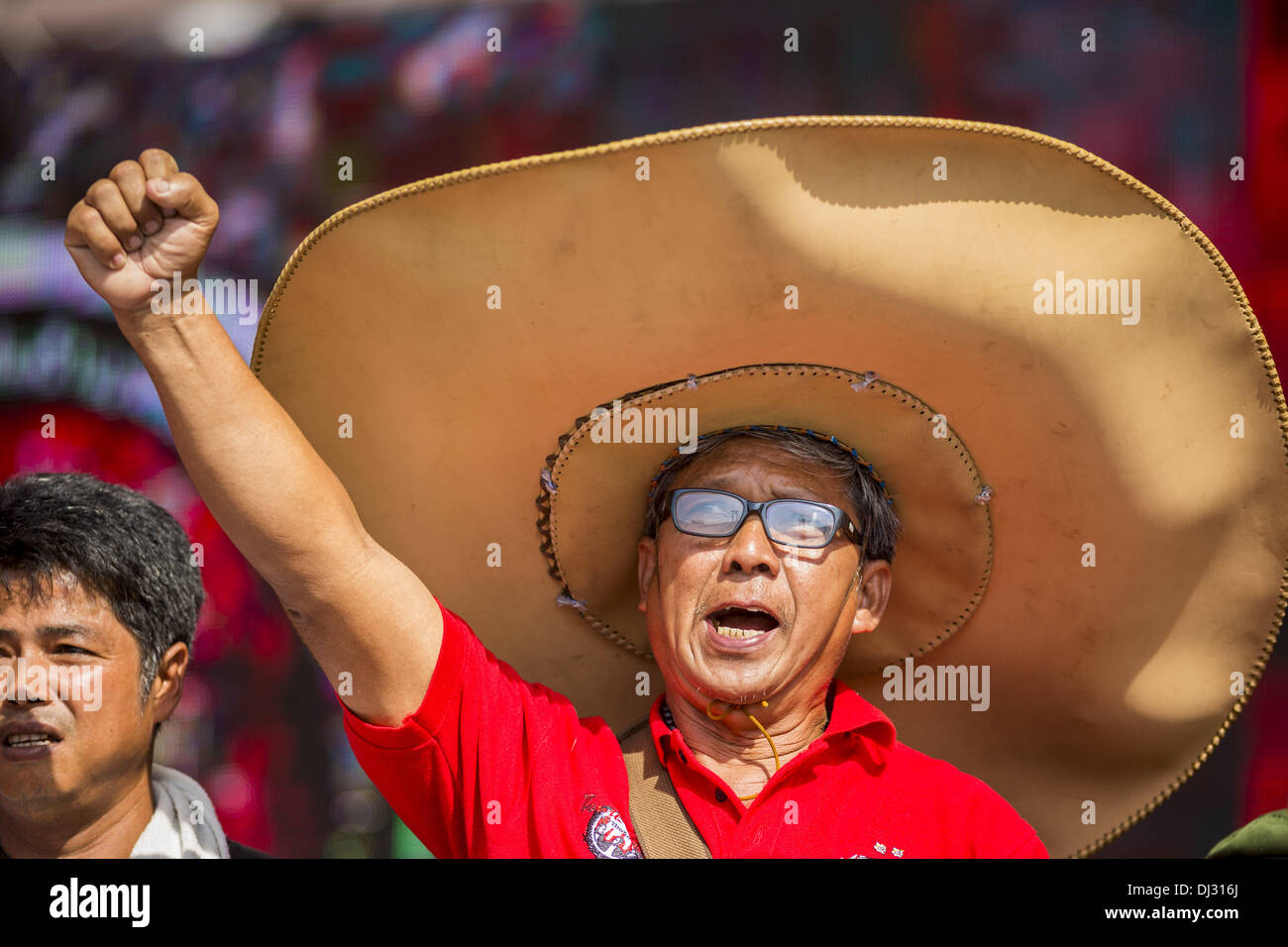 Bangkok, Thailand. 20th Nov, 2013. A Red Shirt supporter wearing a giant  cowboy hat raises a clenched fist in support of the government Wednesday.  Thousands of Red Shirts, supporters of the Pheu