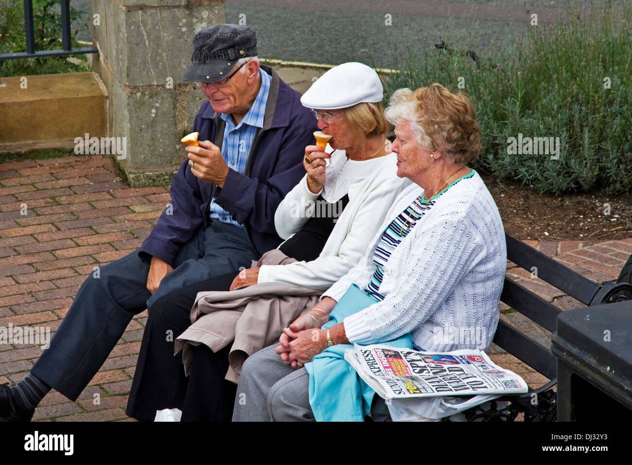 3 older people sitting on bench eating ice cream.  Ironbridge, Shropshire, West Midlands, England, UK Stock Photo