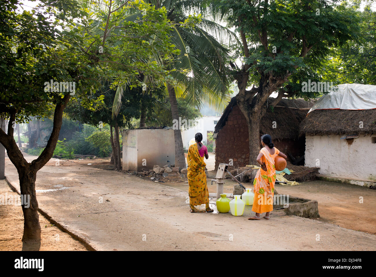 Indian women filling plastic pots with water from a standpipe in a rural Indian village street. Andhra Pradesh, India Stock Photo