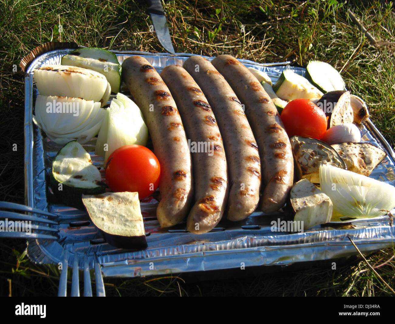 a disposable grill with roasting sausages and grilled vegetables Stock