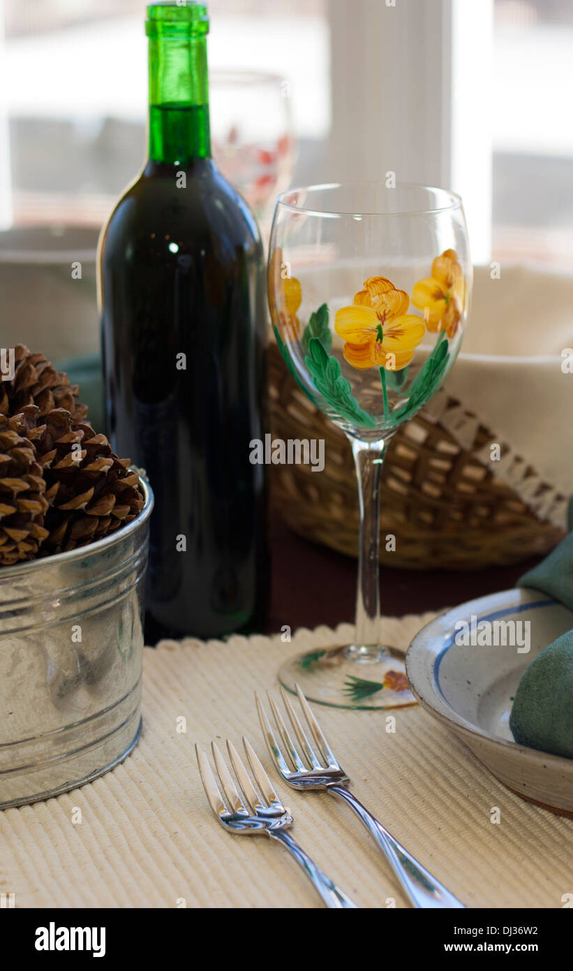 Simple rustic table setting with wicker bread basket, artistic wine glass, and wine bottle, and pottery plate. Stock Photo