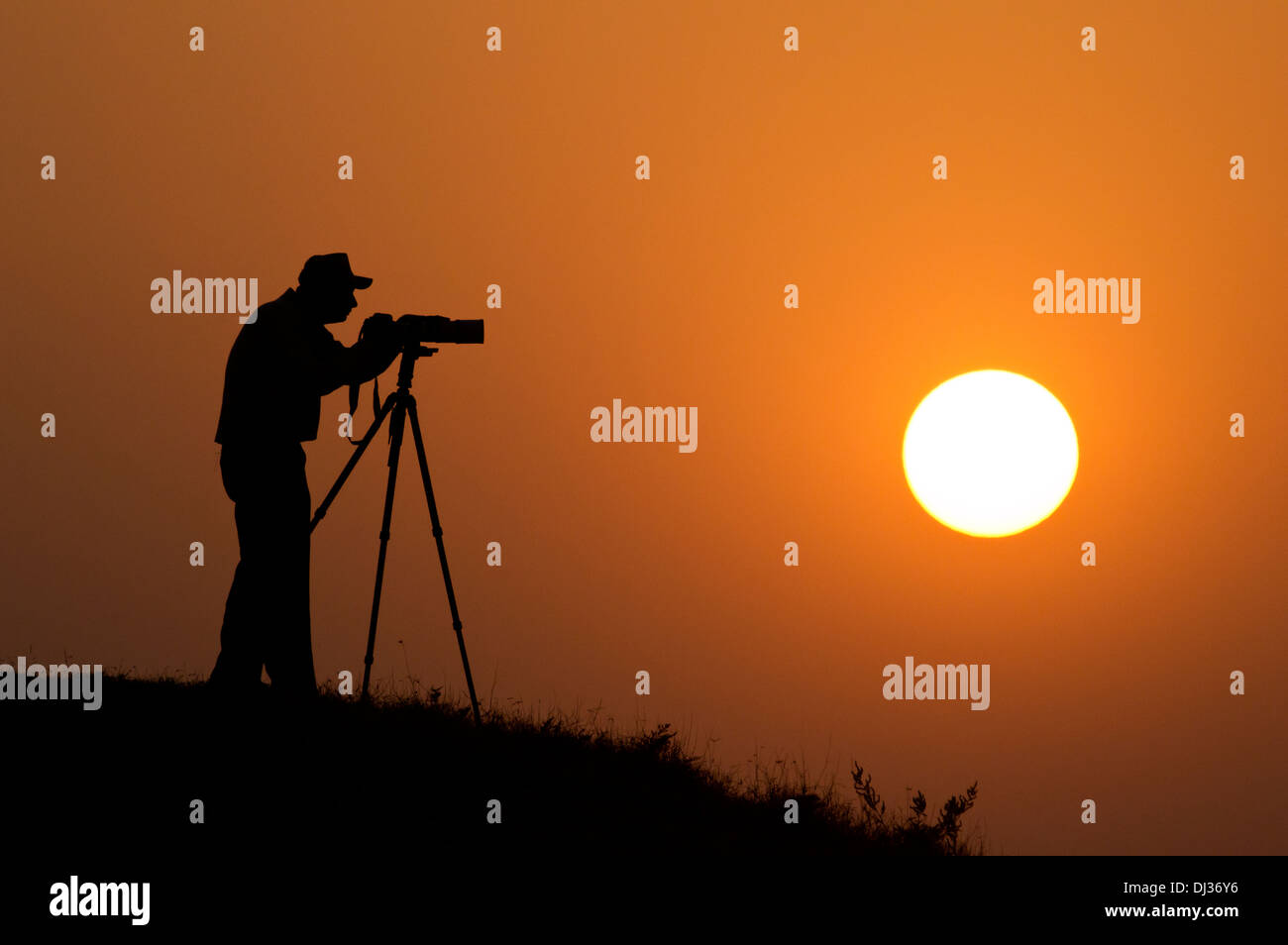 A silhouette of a Photographer with a camera on tripod with the sun in ...