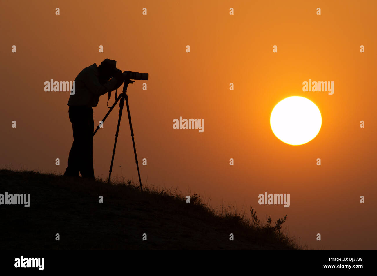 A silhouette of a Photographer with a camera on tripod with the sun in ...