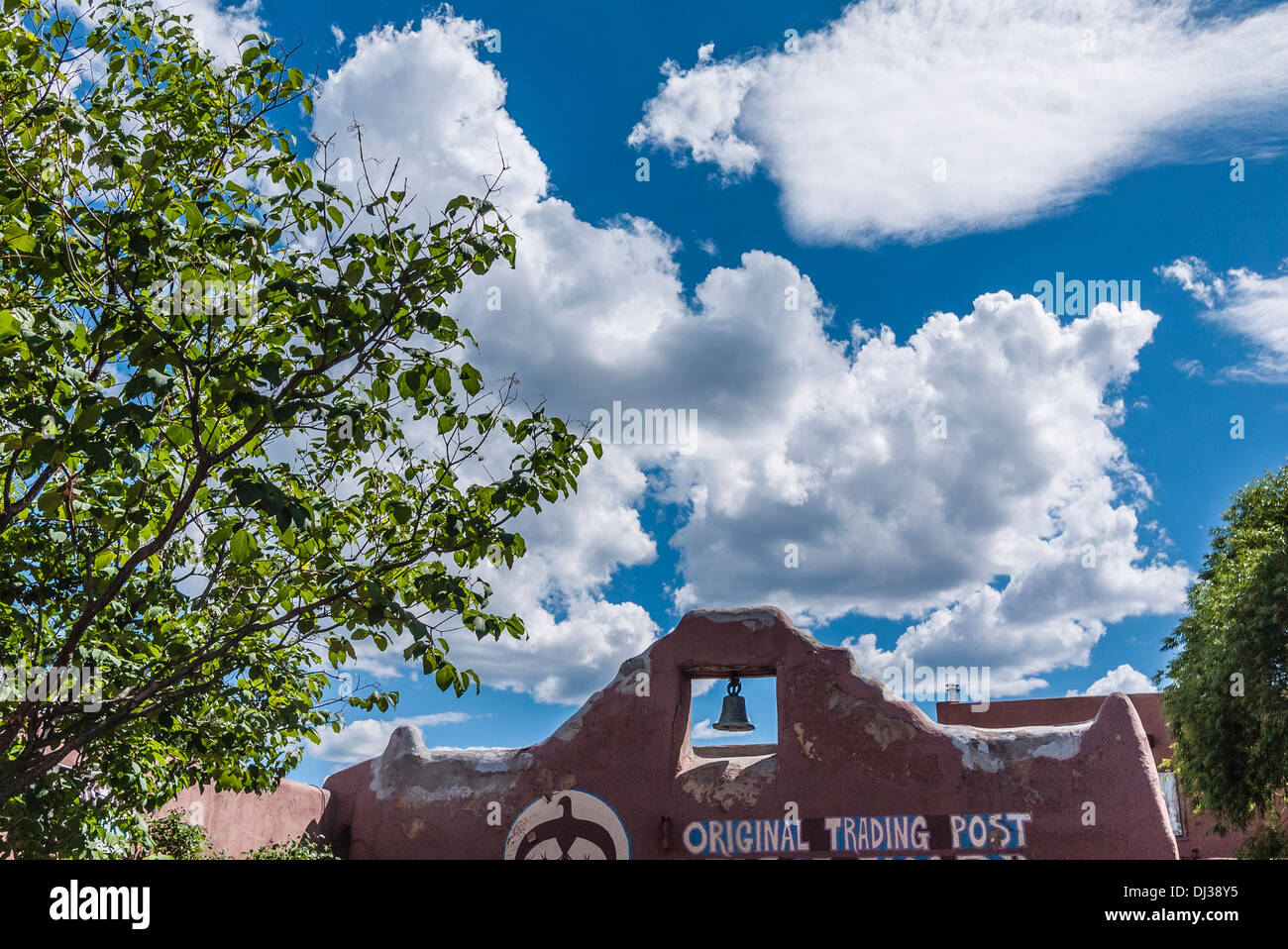 Detail of upper part of front facade of the Original Trading Post of Taos, New Mexico with bell in adobe wall and blue sky. Stock Photo