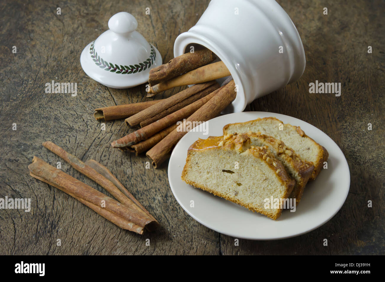 White bowl with cinnamon sticks and slice of banana cake on plate Stock Photo