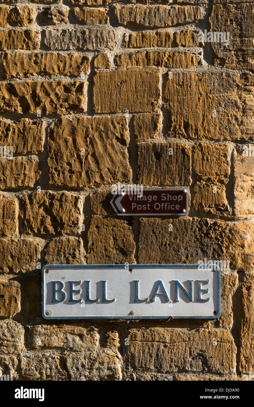 Road name sign and direction sign to the village shop and post office on a cotswold limestone wall in Blockley The cotswolds UK Stock Photo