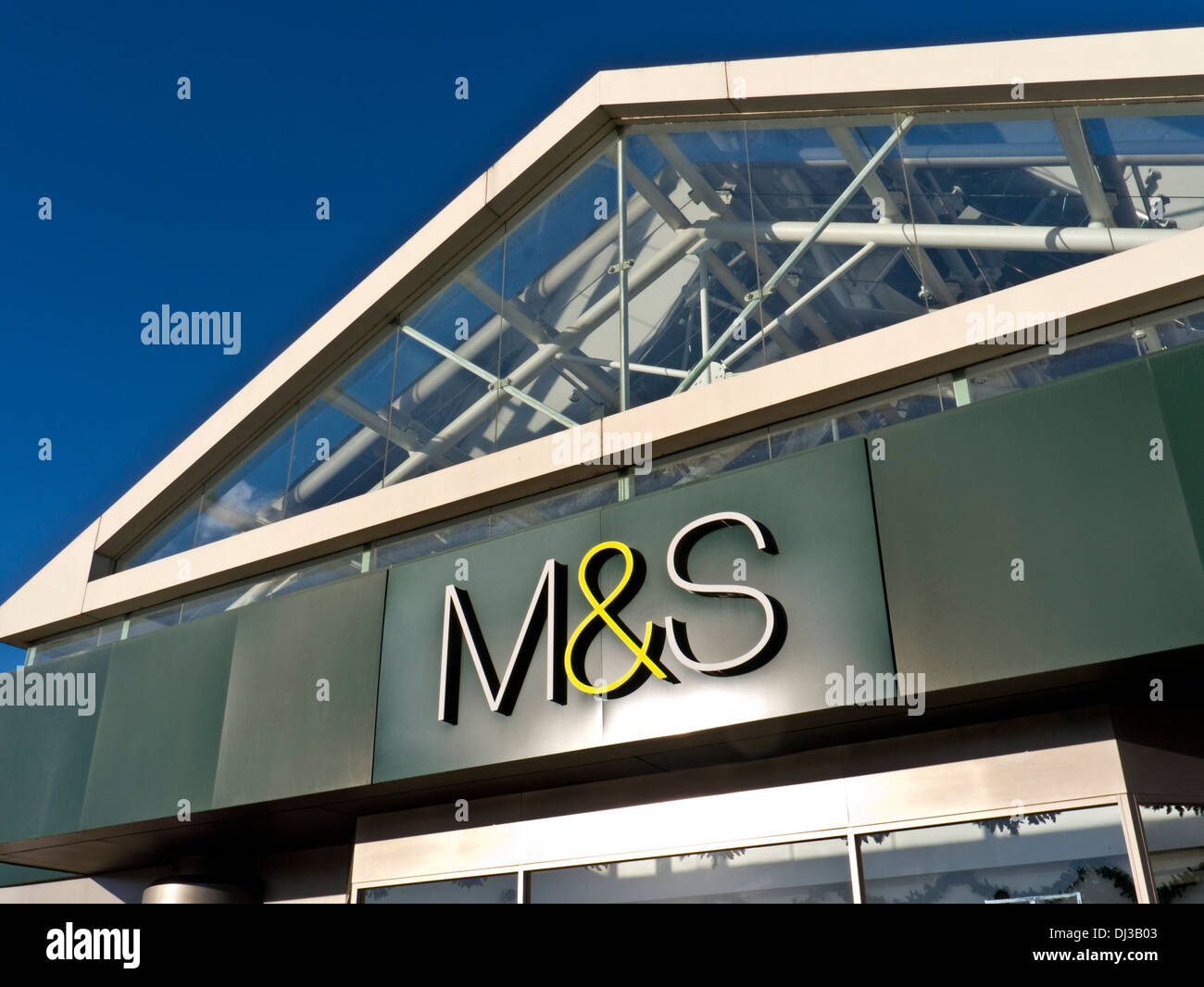 Close view on sunlit reflective M&S logo outside a UK superstore with clear blue sky behind Stock Photo