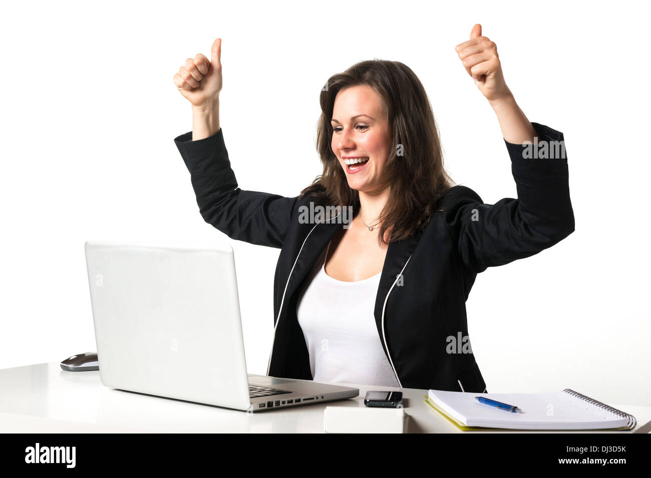 Happy woman sitting in office at desk in front of her laptop and holding her thumbs up Stock Photo