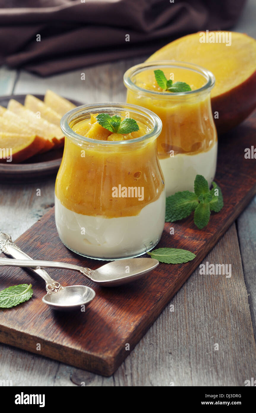Yogurt with mango and mint in glass jars on wooden background Stock Photo