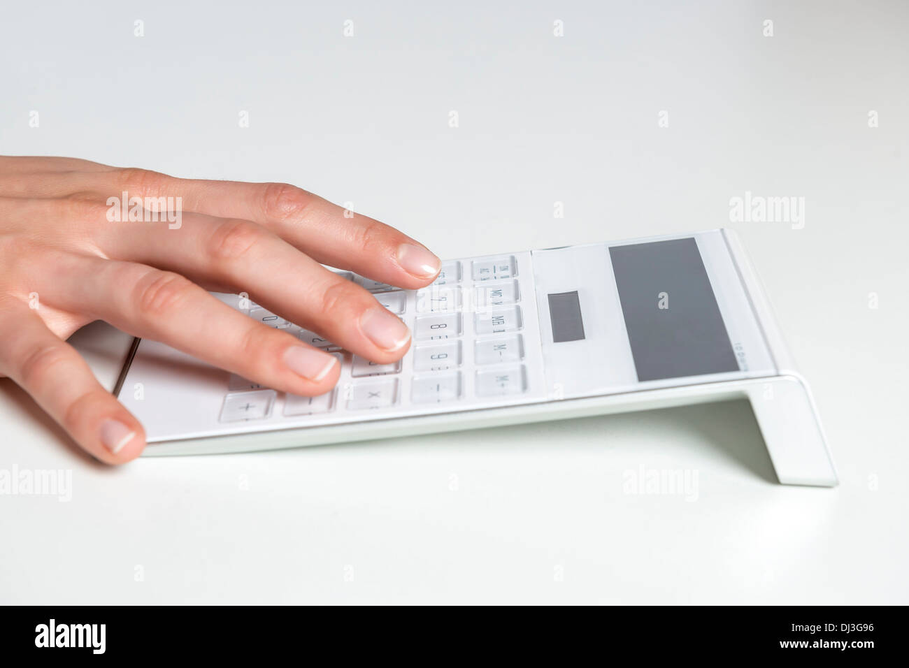 Picture of a female hand typing on a white calculator with empty display Stock Photo
