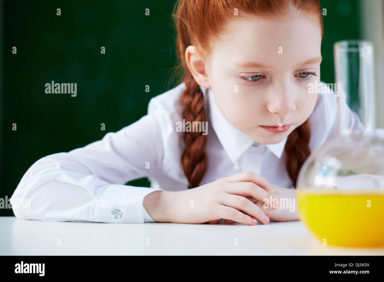 Portrait of serious schoolgirl sitting at workplace and looking at chemical liquid in tube Stock Photo