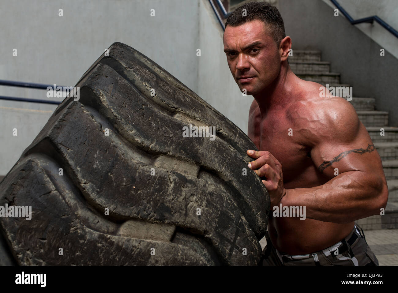 A muscular man participating in a cross fit workout by doing a tire flip Stock Photo
