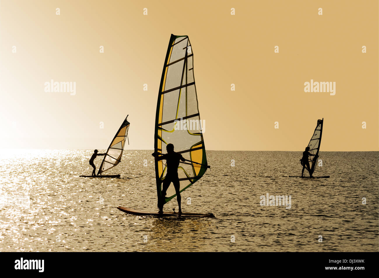 Silhouettes of three windsurfers on waves of a gulf Stock Photo