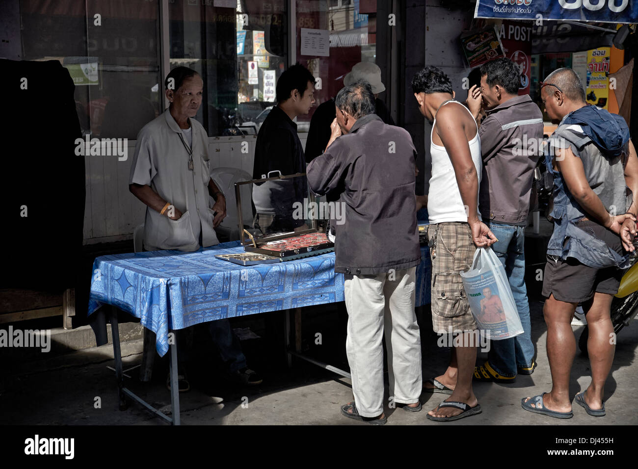 Thailand street scene with people inspecting Buddhist amulets offered for sale by trader. Thailand S. E. Asia Stock Photo