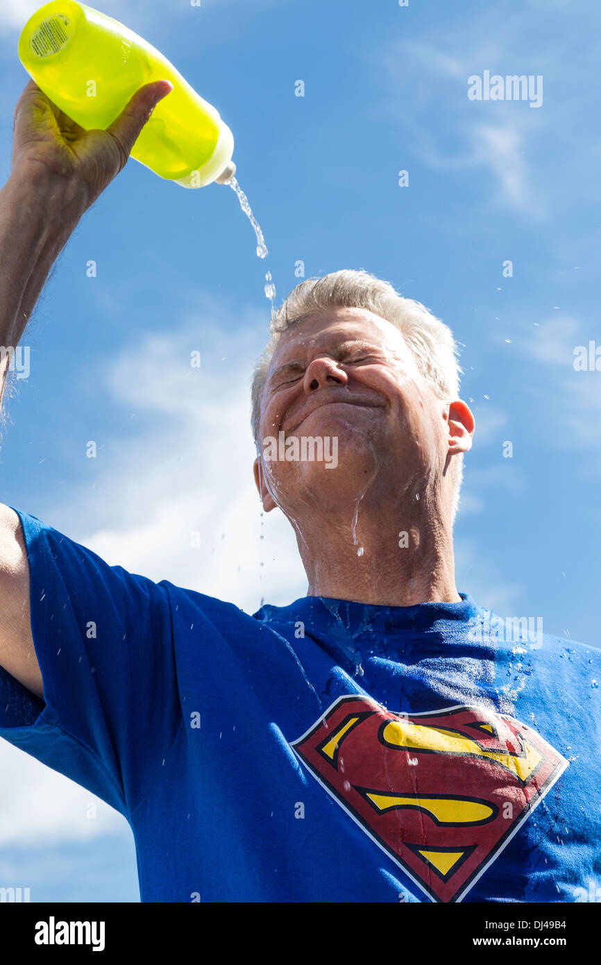 Senior man, wearing superman T-shirt, pouring water over his face to relieve heat exhaustion, United States Stock Photo