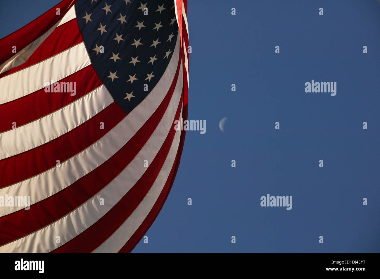 An American Flag waves before a crescent moon Stock Photo