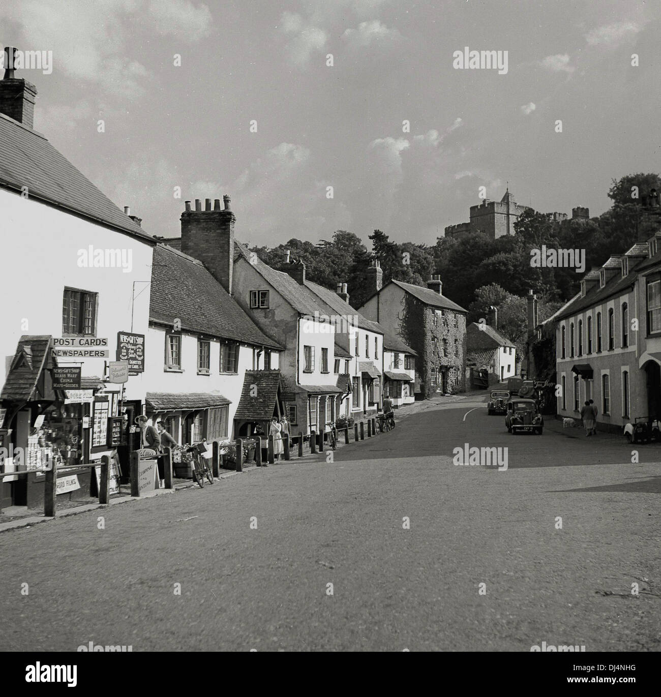 Historical, 1950s, Dunster High Street. Dunster is a old village dating back to medieval times, with ancient castle - seen in the background - priory, dovecote, yarn market, inns and tearooms in Somerset, England. Stock Photo