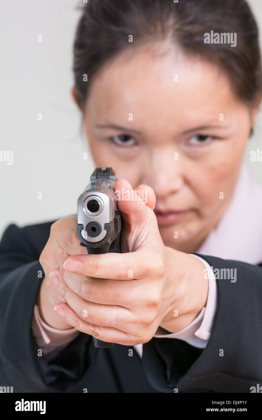 Close up portrait of woman in business suit aiming a hand gun at you Stock Photo