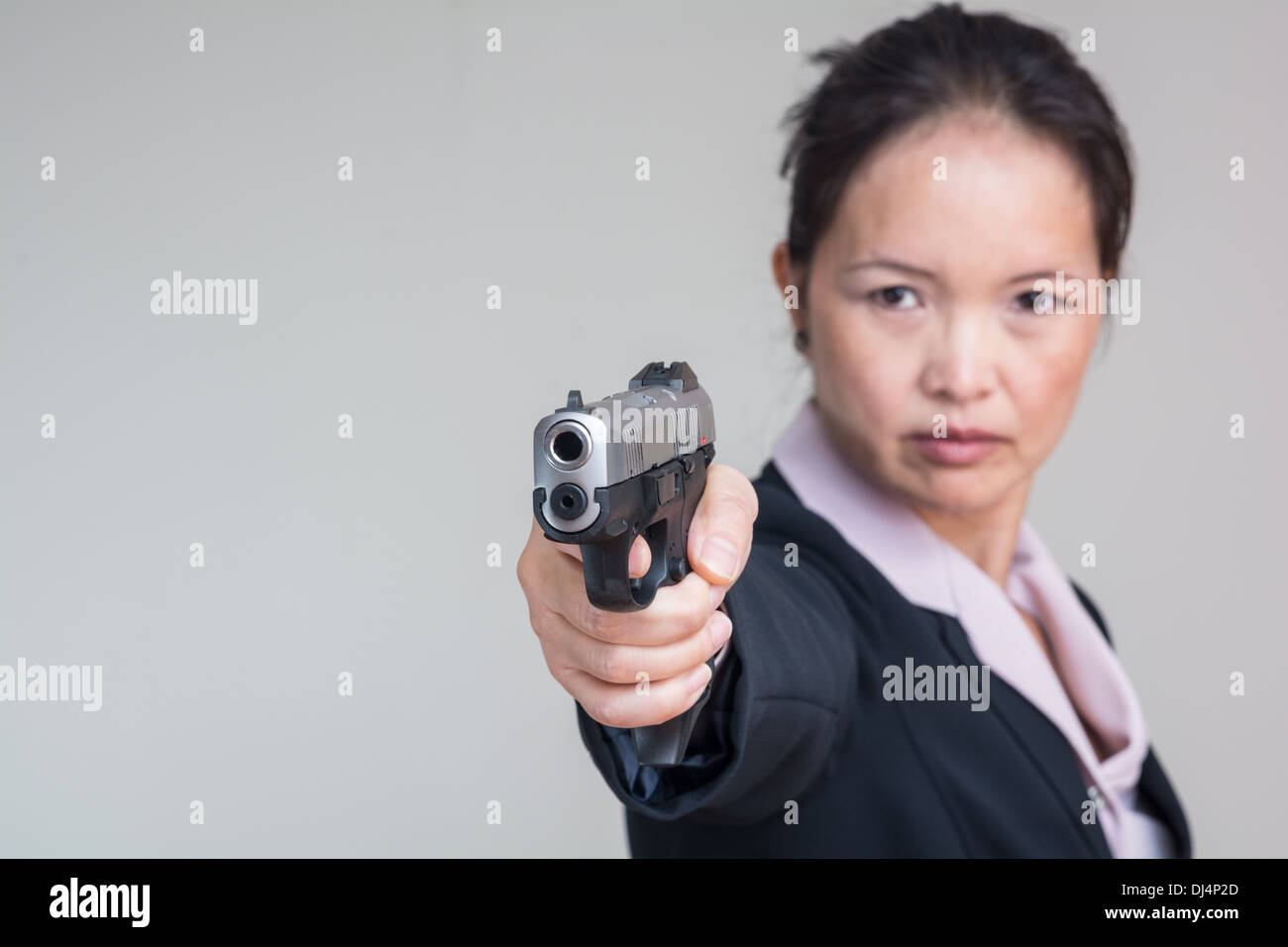 Close up portrait of woman in business suit aiming a hand gun Stock Photo