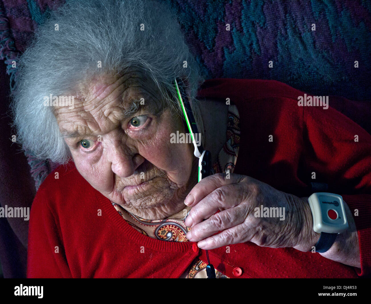 Vulnerable isolating covid-19 elderly old senior lady wearing an emergency call button alone at home talks anxiously on her telephone Stock Photo