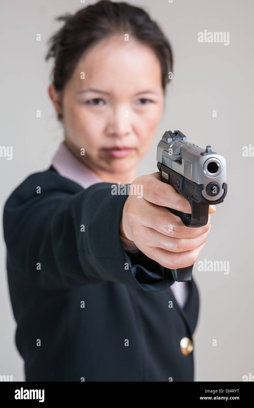 Close up portrait of woman in business suit aiming a hand gun Stock Photo