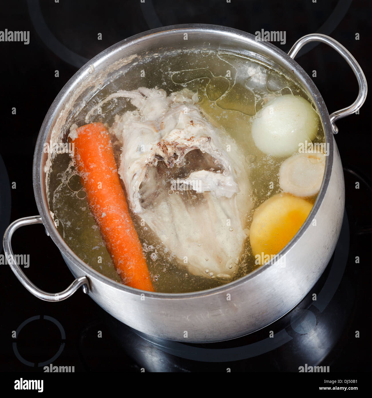 top view of boiling chicken broth with seasoning vegetables in steel pan on glass ceramic cooker Stock Photo