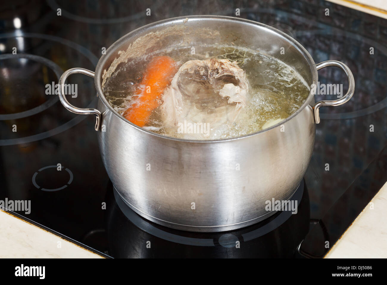 simmering chicken soup with seasoning vegetables in steel pot on glass ceramic cooker Stock Photo