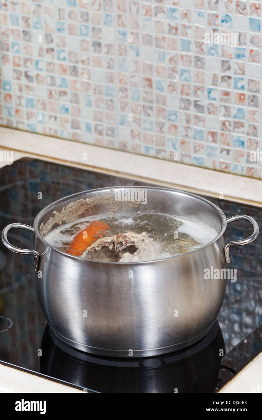 simmering chicken broth with seasoning vegetables in steel pot on glass ceramic cooker Stock Photo