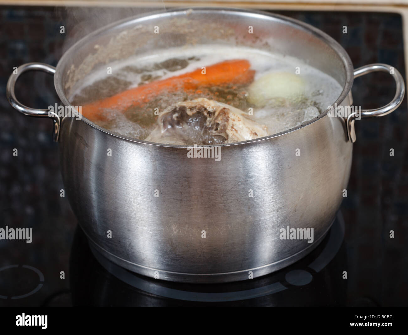 simmering chicken soup in steel pot on glass ceramic cooker close up Stock Photo