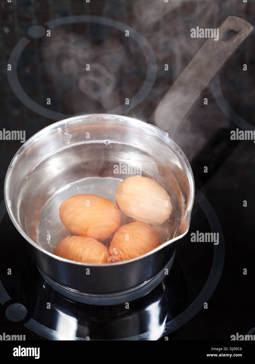 simmering chicken eggs in metal pot on electric stove in kitchen Stock Photo