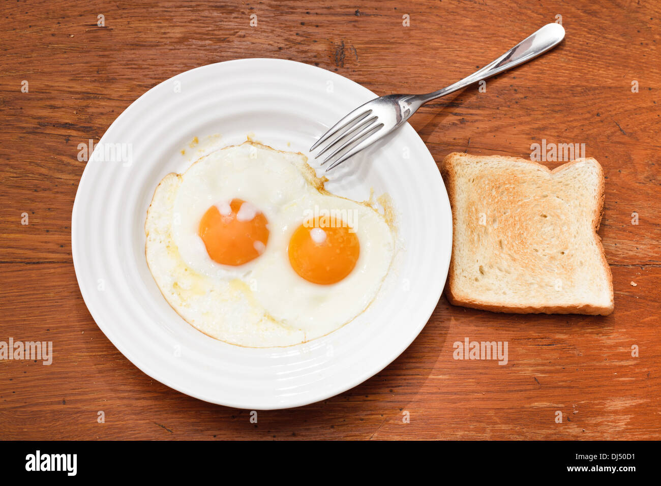 breakfast with two fried eggs on white plate, fresh toast on wooden table Stock Photo