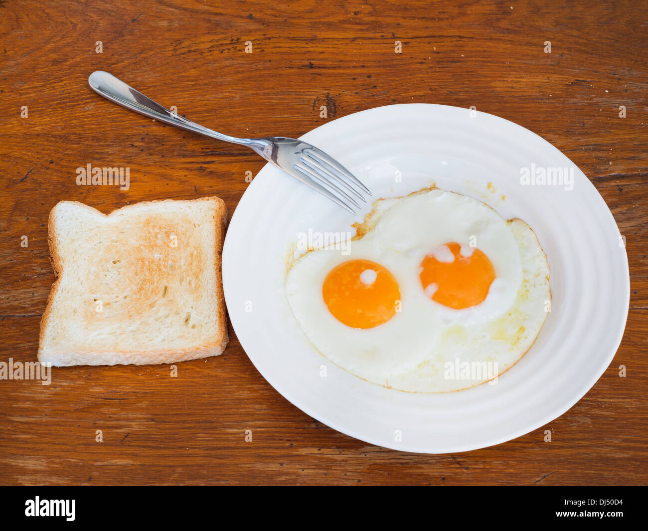 breakfast with two fried eggs on white plate and toast on wooden table Stock Photo