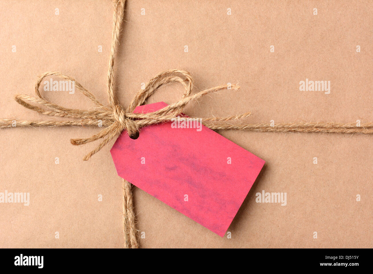 Closeup of a gift tag on a Christmas present. The package is wrapped in plain brown paper and twine. The red tag is blank. Stock Photo