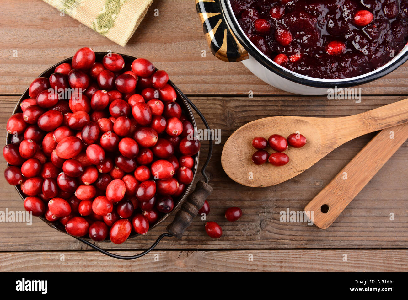 Overhead of a bucket of cranberries and a pot full of whole cranberry sauce on a rustic wooden table. Stock Photo
