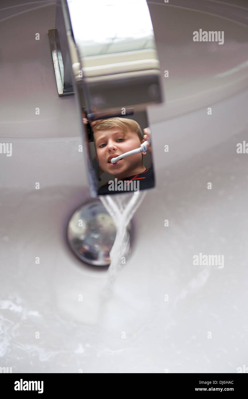 A reflection of a young boy brushing his teeth at a bathroom sink. Stock Photo