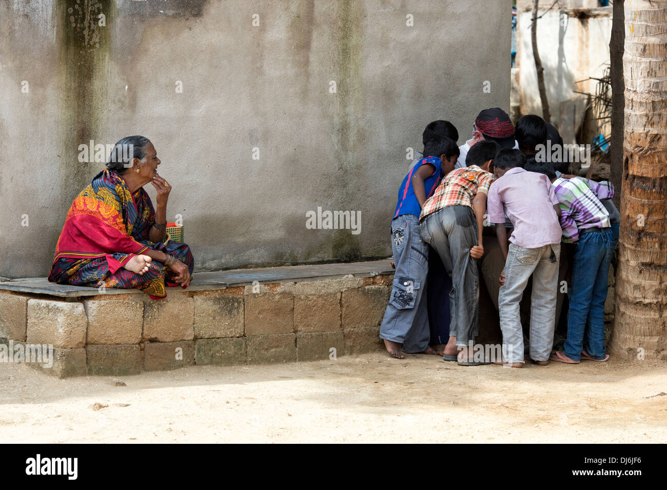 Rural indian boys huddled over a tourists camera watched by an old indian woman.   Andhra Pradesh, India Stock Photo