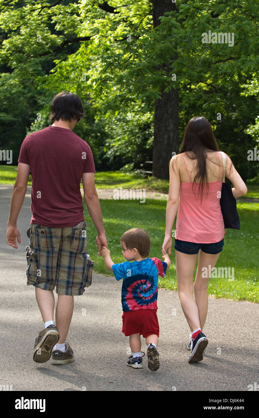 Young Couple Holding Hands of Toddler Son and Walking on Path in Spring Mill State Park in Indiana Stock Photo