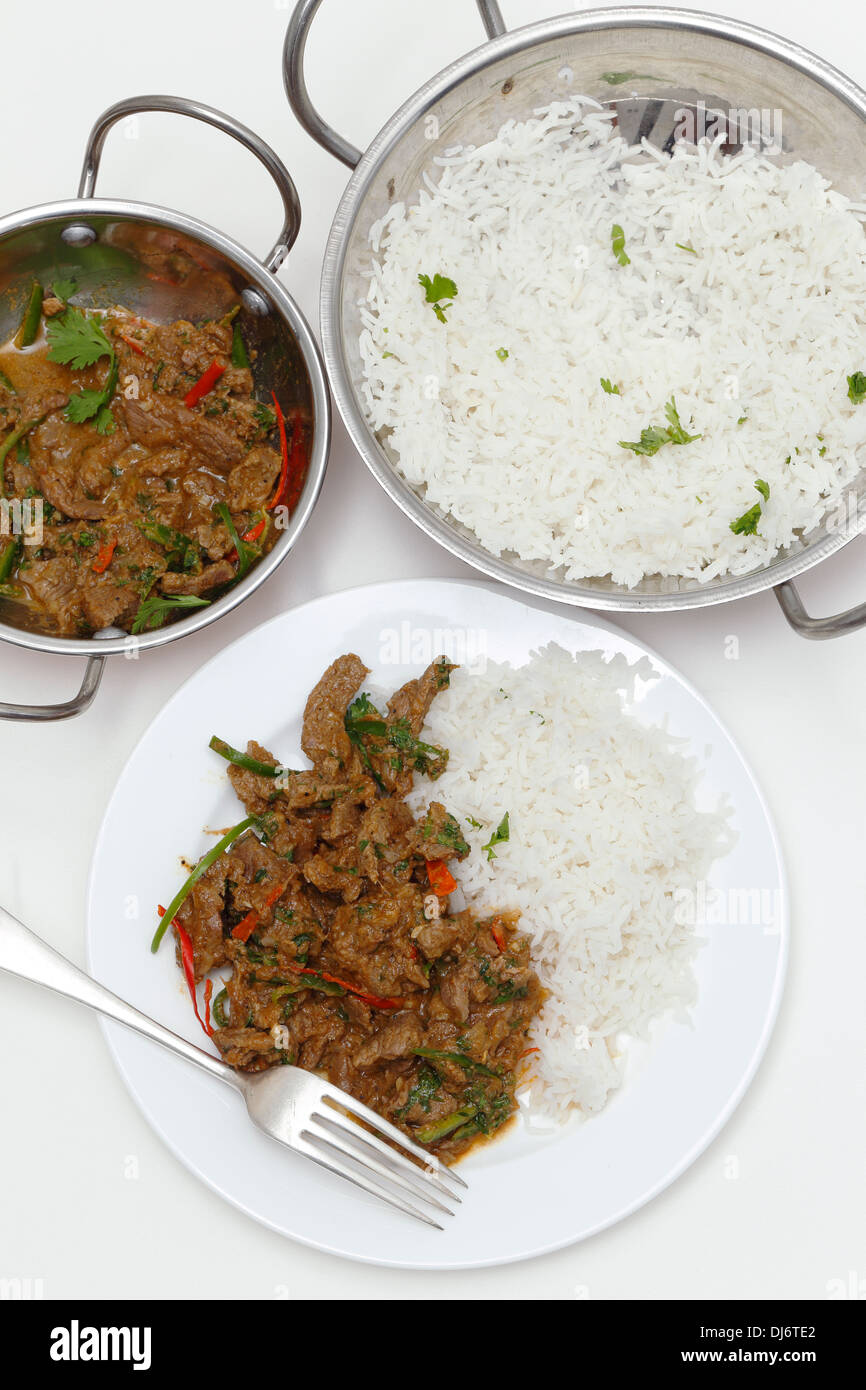 A bowl of spiced lamb curry with coriander leaves and chillies, next to