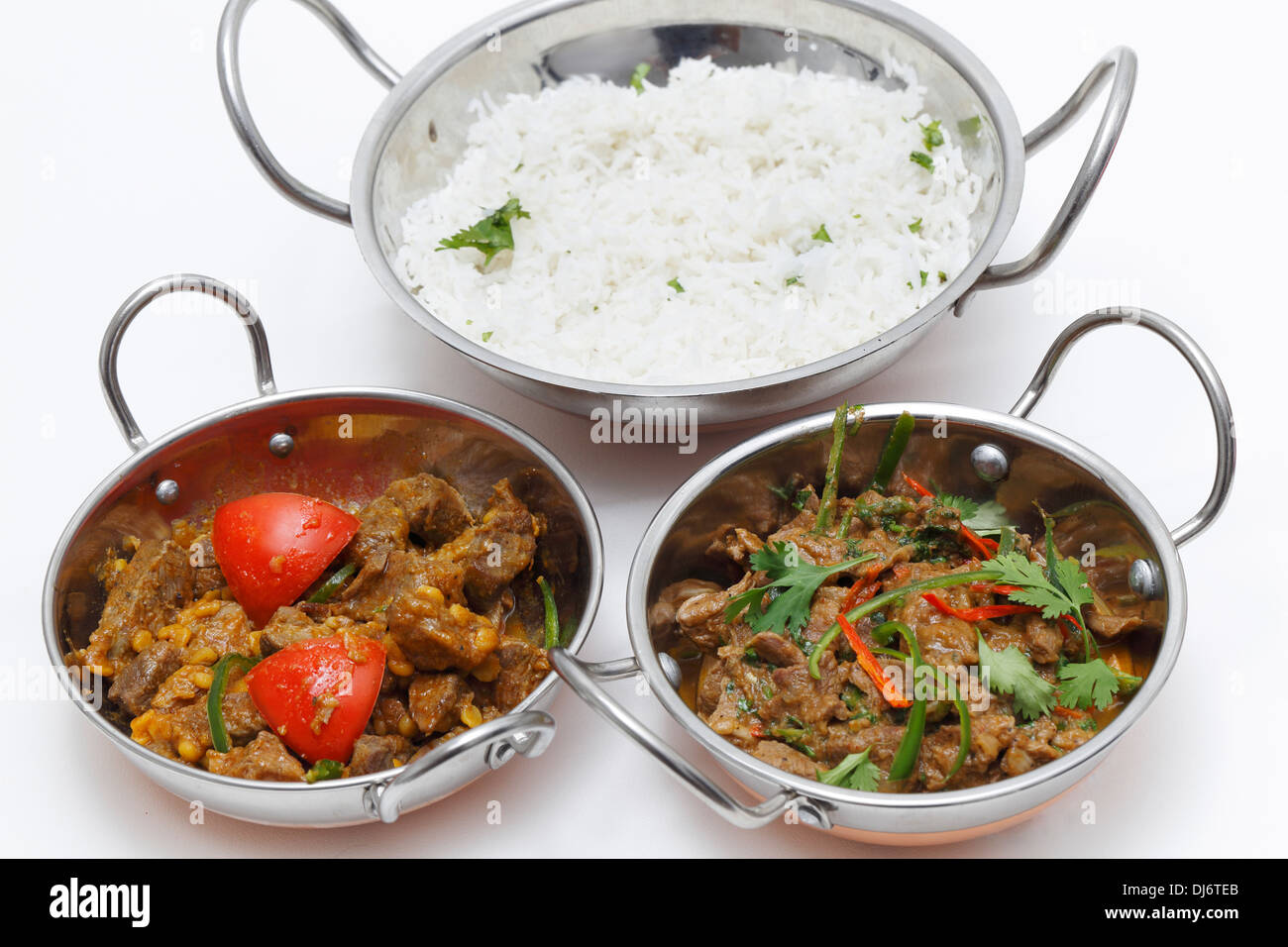 A bowl of spiced lamb curry with coriander leaves and chillies, next to
