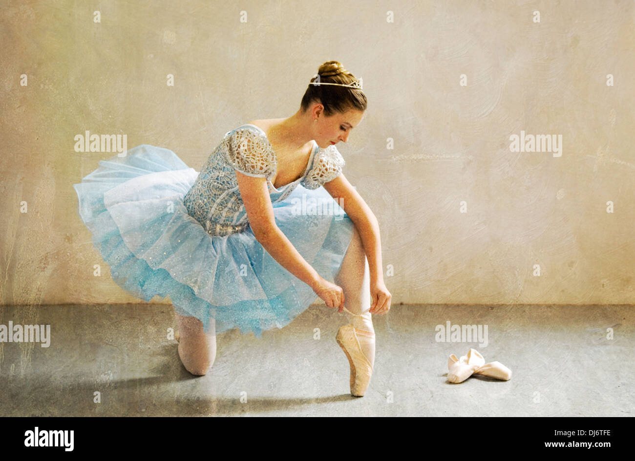 Young Ballerina Sitting on the Floor of a Studio Tying Her Ballet Slippers Stock Photo