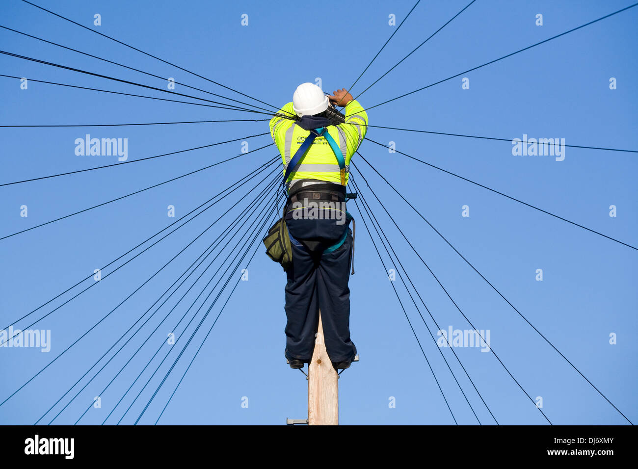 BT plc Telecom engineer (British Telecom PLC) installs a new domestic phone line and broadband internet copper wire to a telephone / telegraph pole in a London Street / Road, under a blue sky. © David Gee 4 Stock Photo