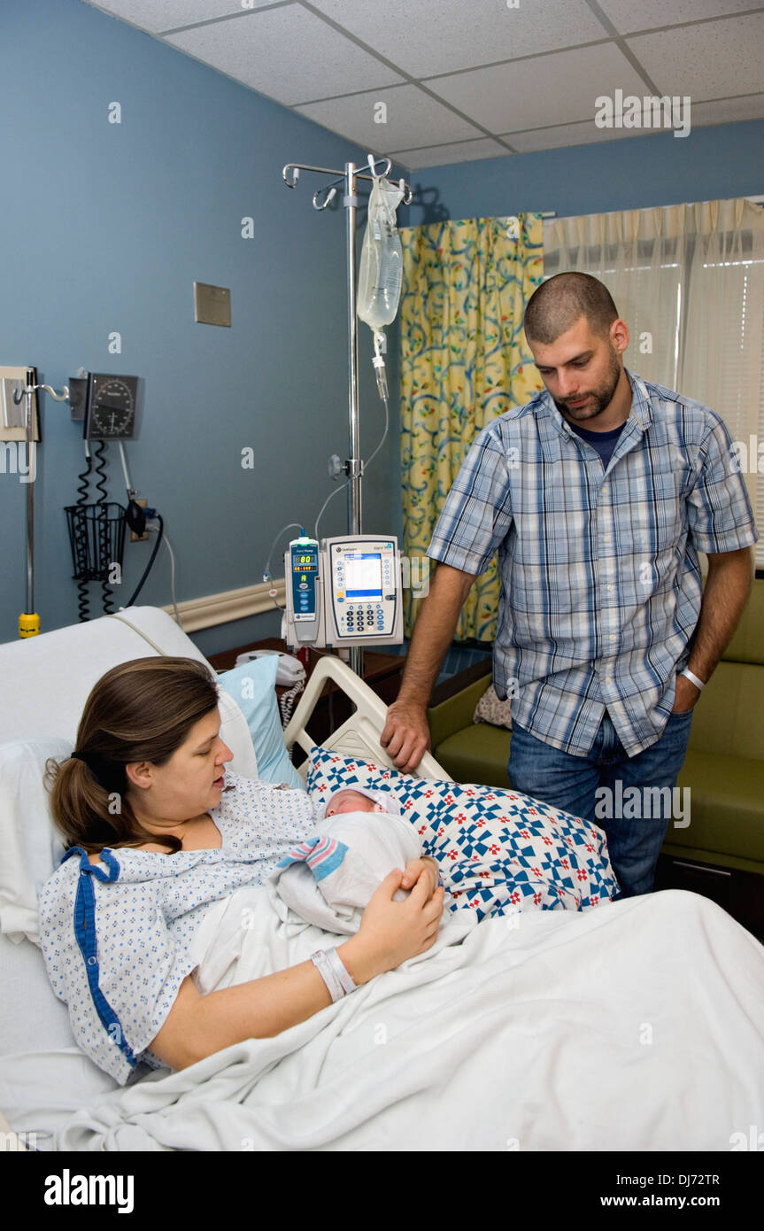 Woman Holding Her Newborn Baby in the Hospital while Husband Watches Stock Photo