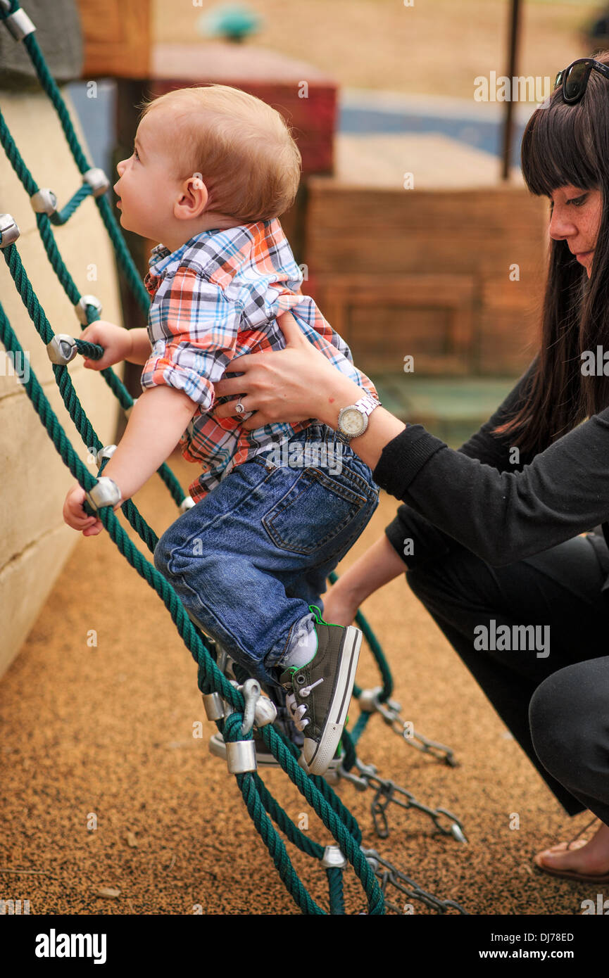 A young toddler strives to climb the ladder to reach the next level. He has the help of others. Stock Photo