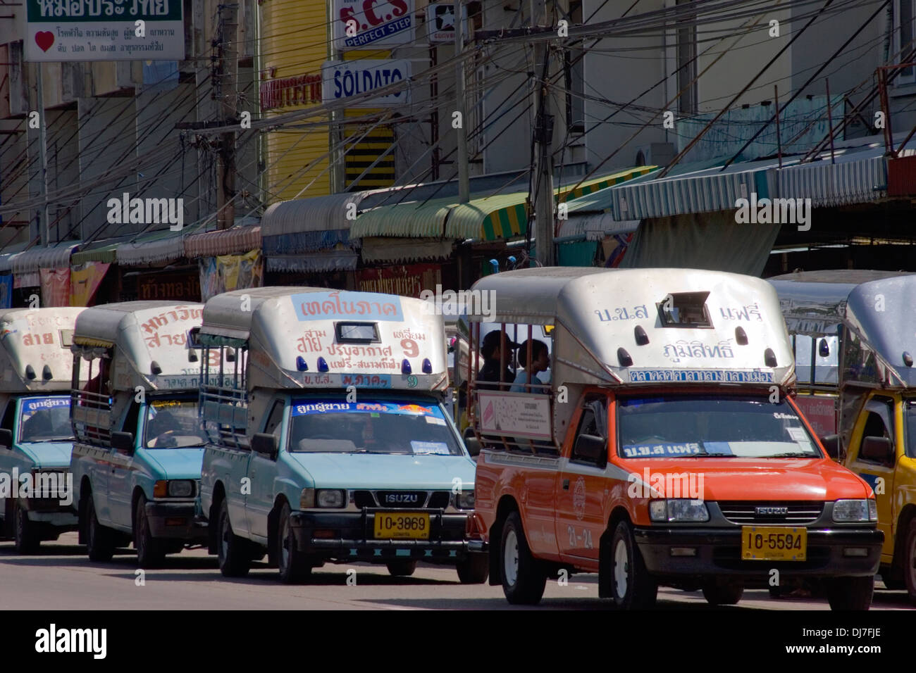 A row of songthaews (taxis) are parked in a row near a shopping area on a city street in Khon Kaen, Thailand. Stock Photo