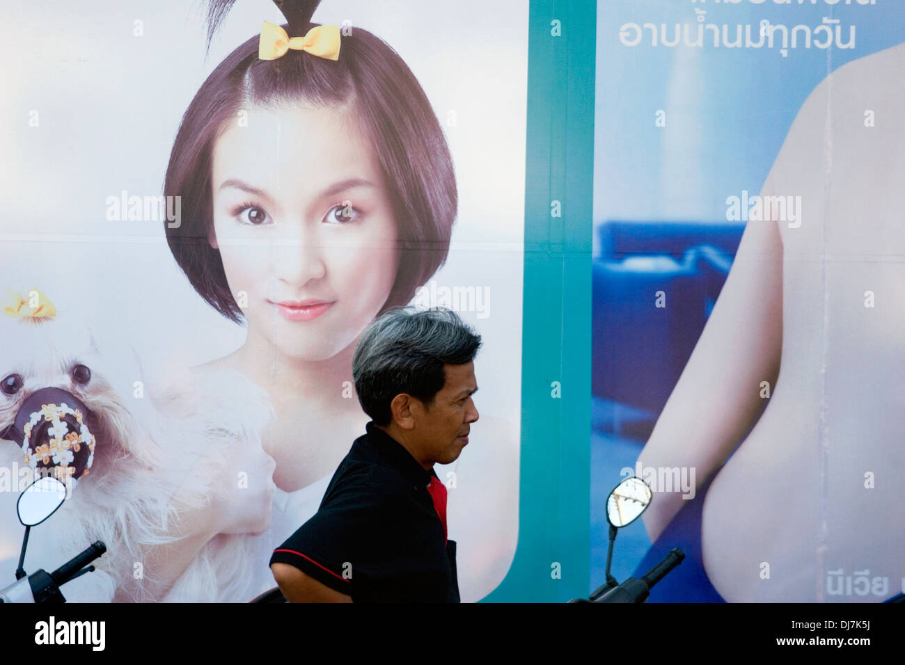 A man is walking past a sign with a young model advertising a product on a city street in Khon Kaen, Thailand. Stock Photo