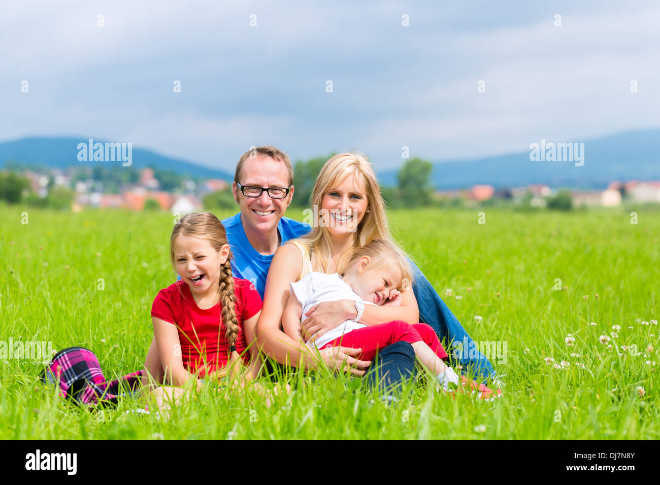 Happy family of Mother, father and kids or daughter and sisters or siblings sitting outdoor on meadow Stock Photo