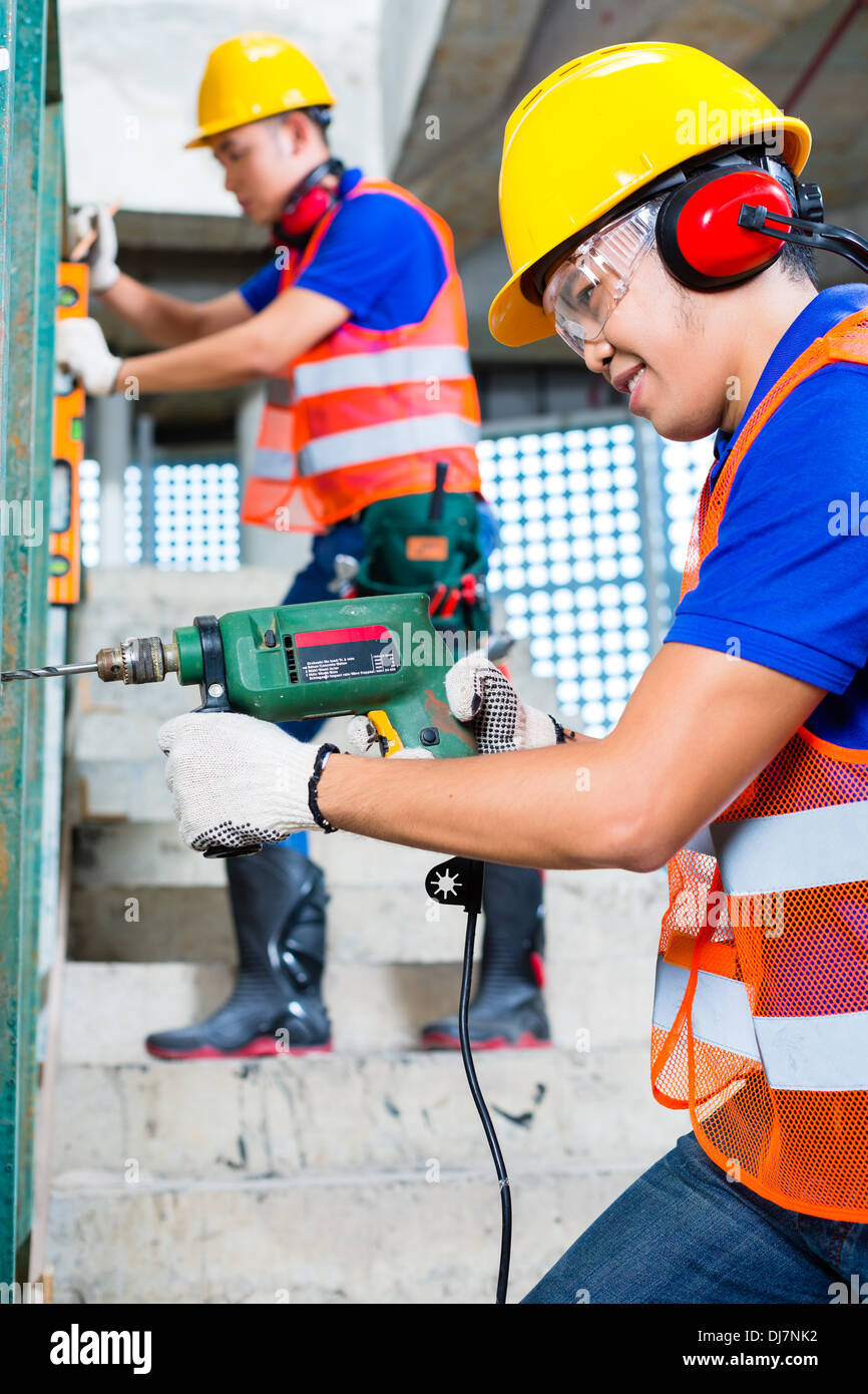 Asian Indonesian construction site workers drilling with a machine or