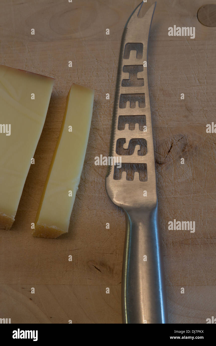 A photograph of some Swiss cheese with a cheese knife on a wooden cutting board. It is Gruyere cheese. Stock Photo