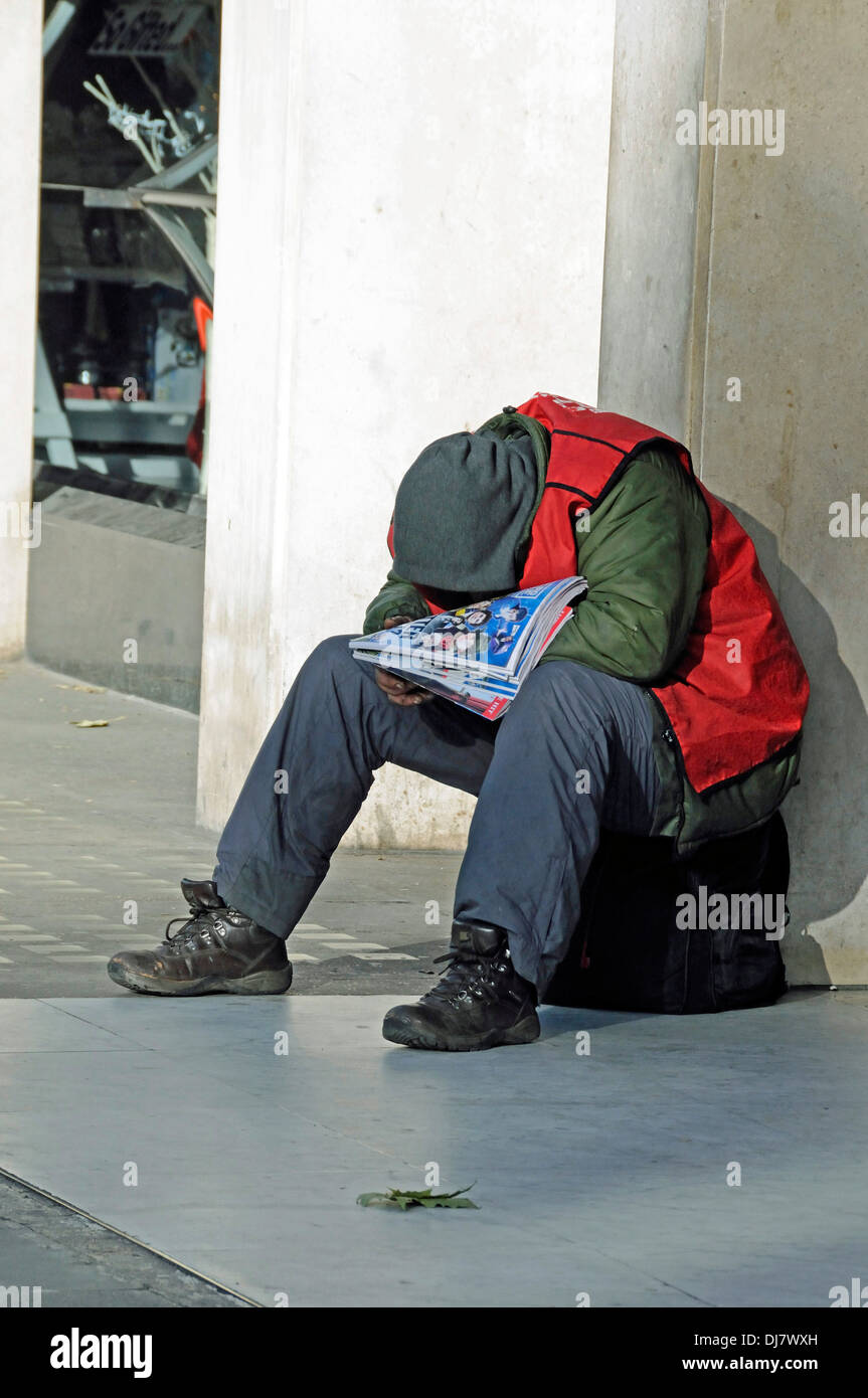 Big issue seller wrapped up against the cold and asleep in the sunshine, Central London, England UK Stock Photo